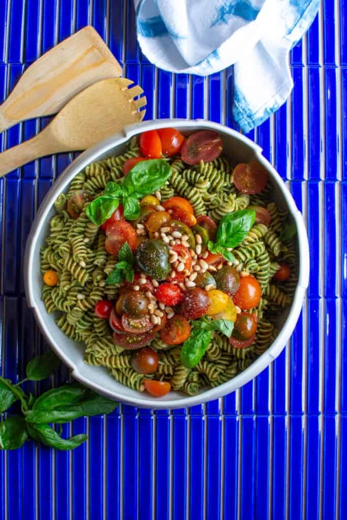A bowl of whole wheat pasta salad on a blue tile table. 