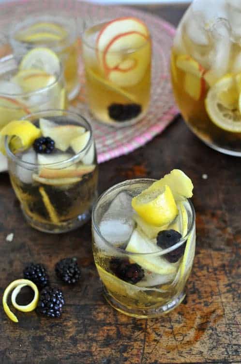 Several glasses of white sangria with apple slices and blackberries.