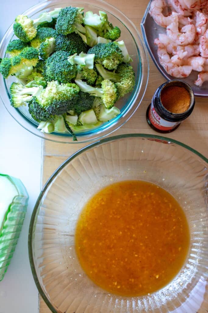 The marinade in a large glass bowl with broccoli and shrimp