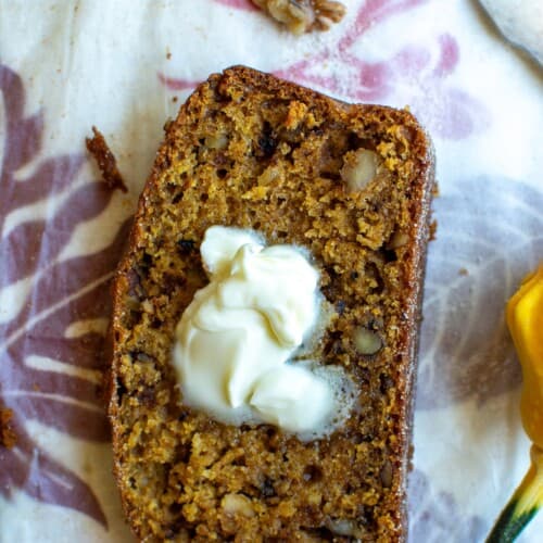 A piece of pumpkin walnut bread with butter on it.