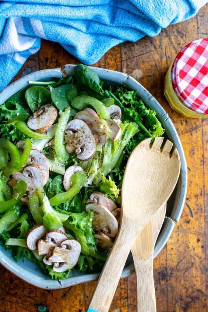 a spinach salad with two wooden spoons in the bowl