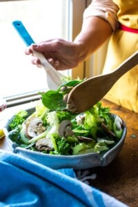 A woman tossing a spinach salad with two wooden spoons
