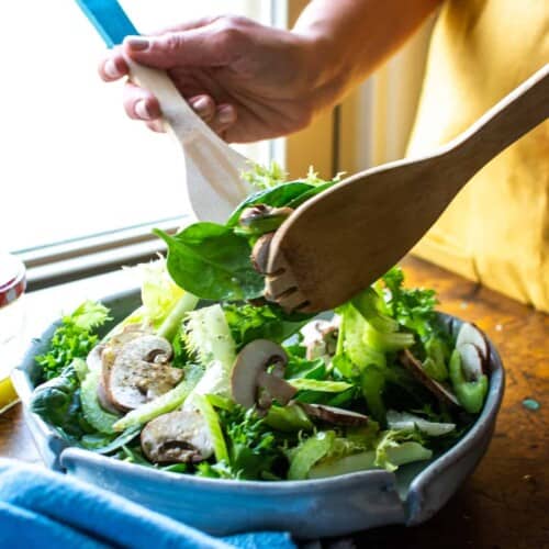A woman tossing a spinach salad with two wooden spoons