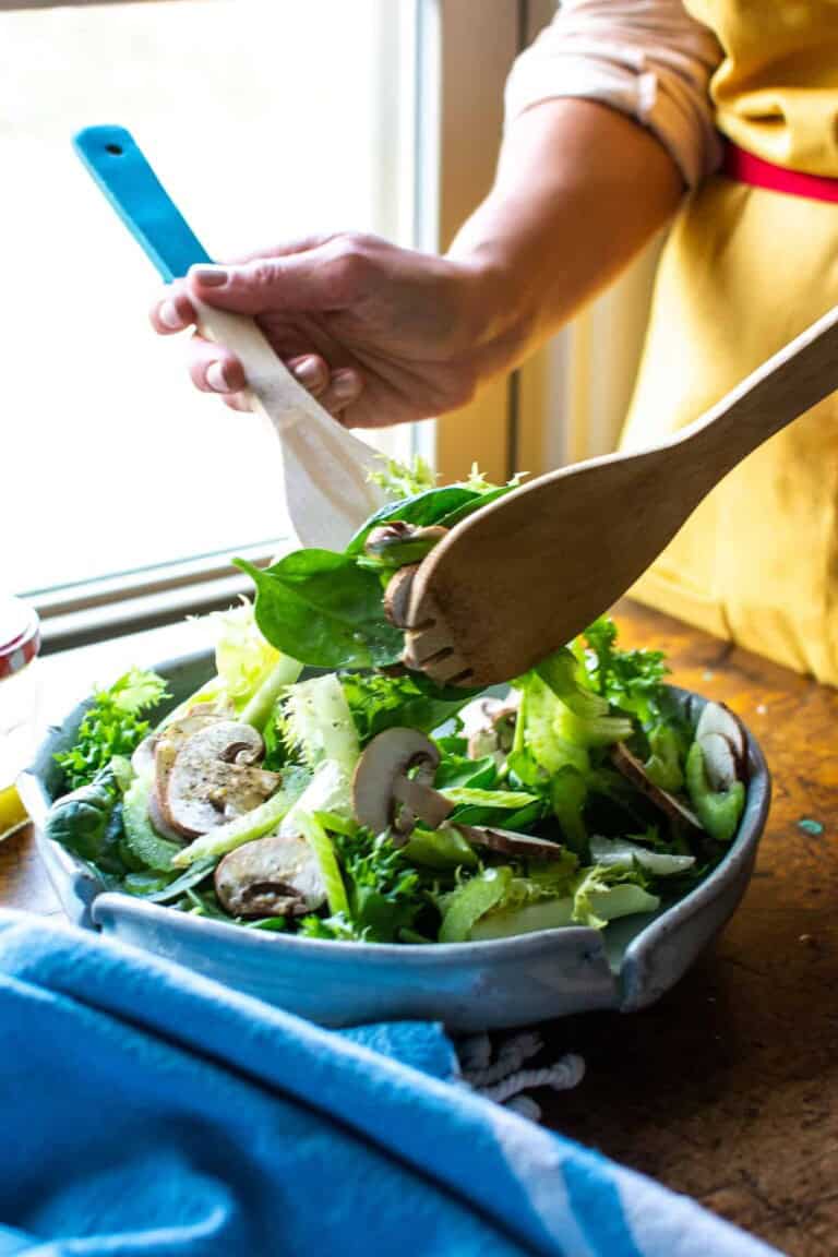 A woman tossing a spinach salad with two wooden spoons