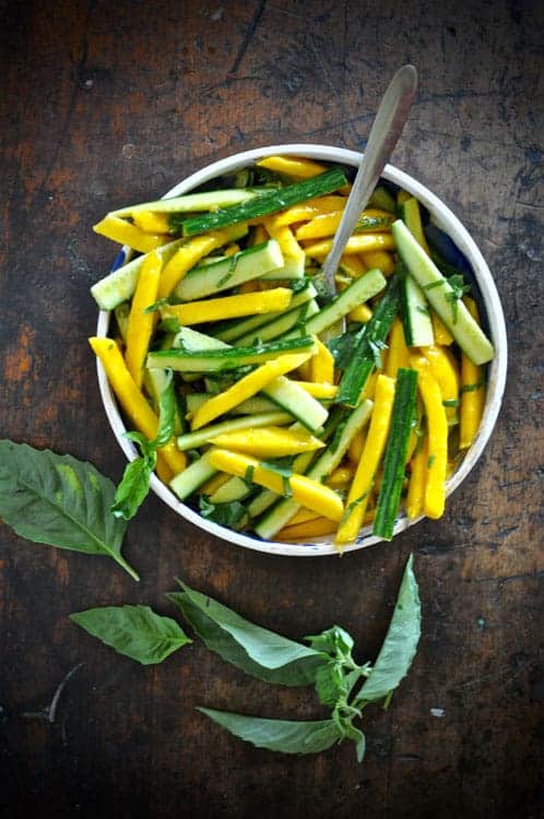 a mango and cucumber salad on a wood table.