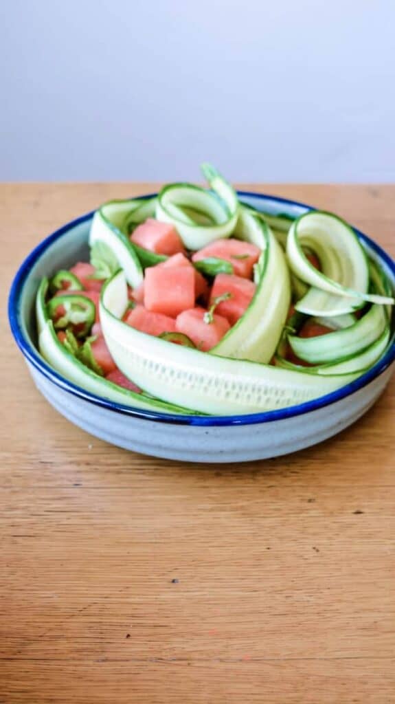 cucumber and watermelon in a bowl on a wood table.