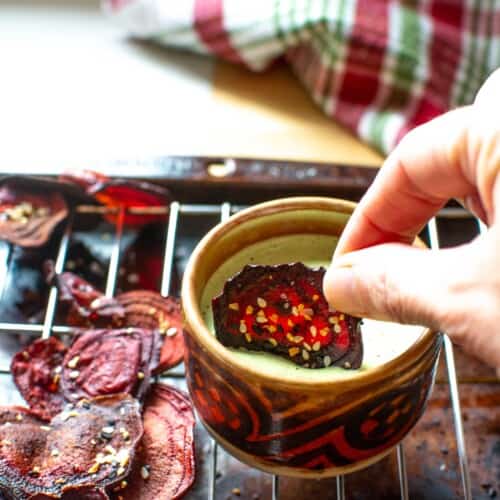 a beet chip being dipped into a green dip
