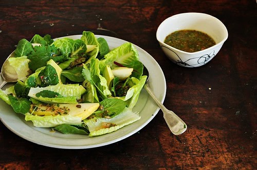 a salad on a plate with a bowl of dressing next to it. 