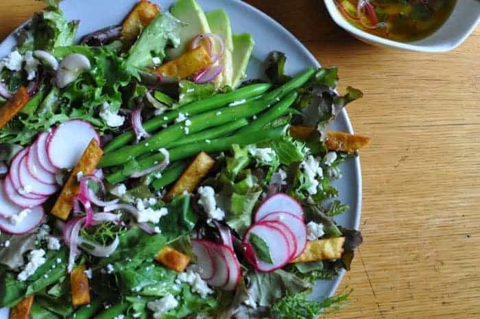 A large plate of salad with slices of radish