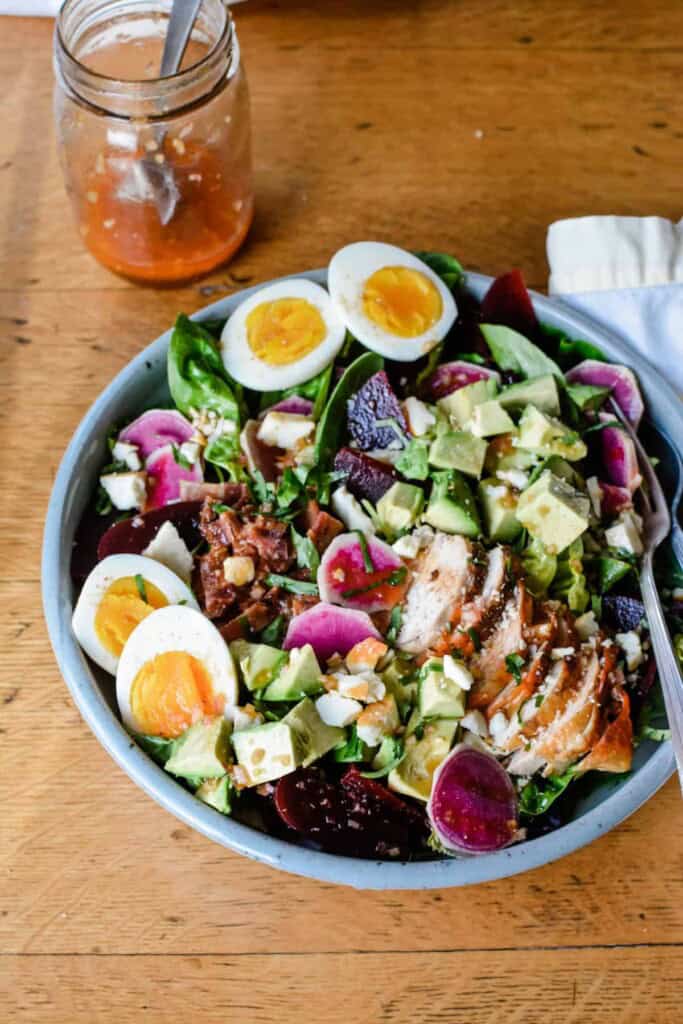 A salad with hard boiled eggs on top next to a bottle of dressing.