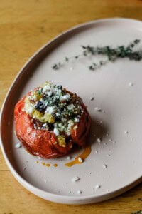 A tomato stuffed with orzo and ham on a pink plate