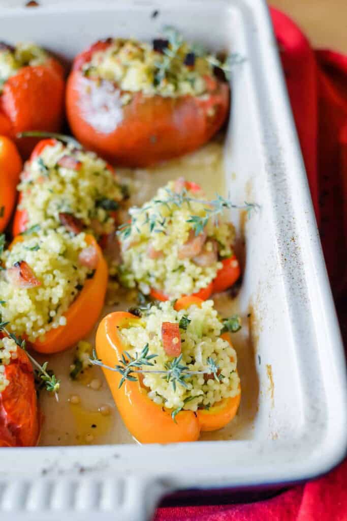 peppers and tomatoes in a baking dish stuffed with orzo and ham.