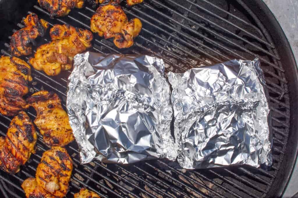 foil packets on a grill next to potatoes