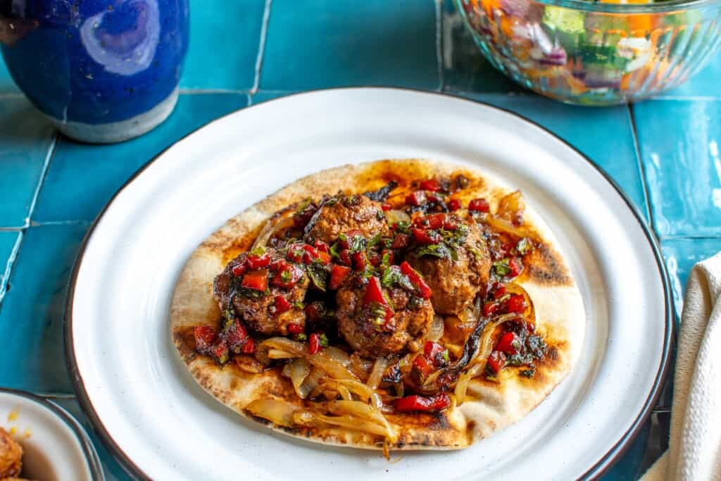 turkish meatballs on a white plate with onions and pita