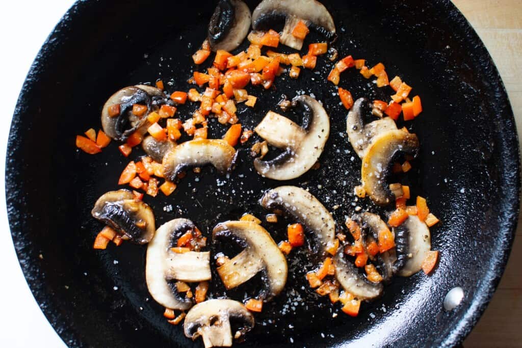 mushrooms and peppers sauteeing in a black pan