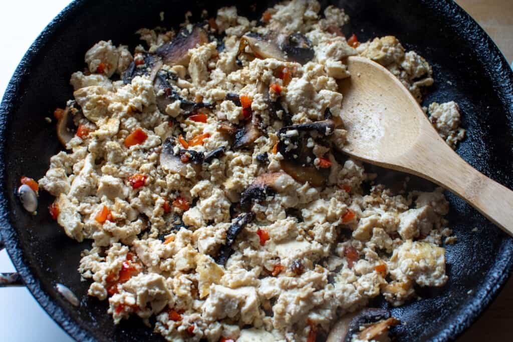 tofu and vegetables in a black pan with a wooden spoon