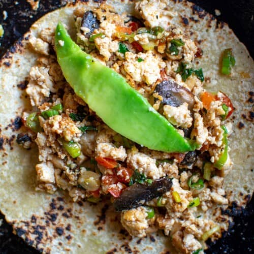 a tortilla with scramble on top and a piece of avocado