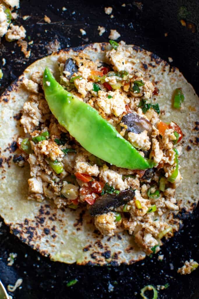a tortilla with scramble on top and a piece of avocado