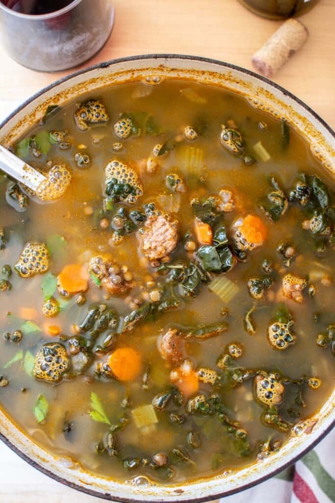 lentil soup in a pot next to a glass of wine