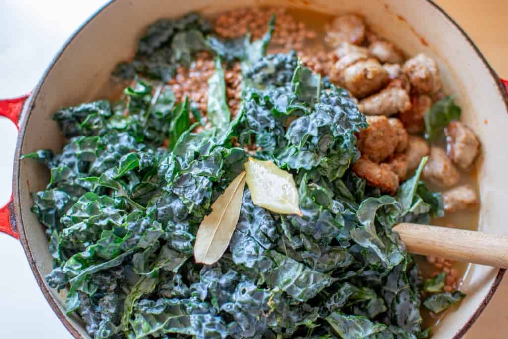 kale and bay leaves in a soup pot with a wooden spoon