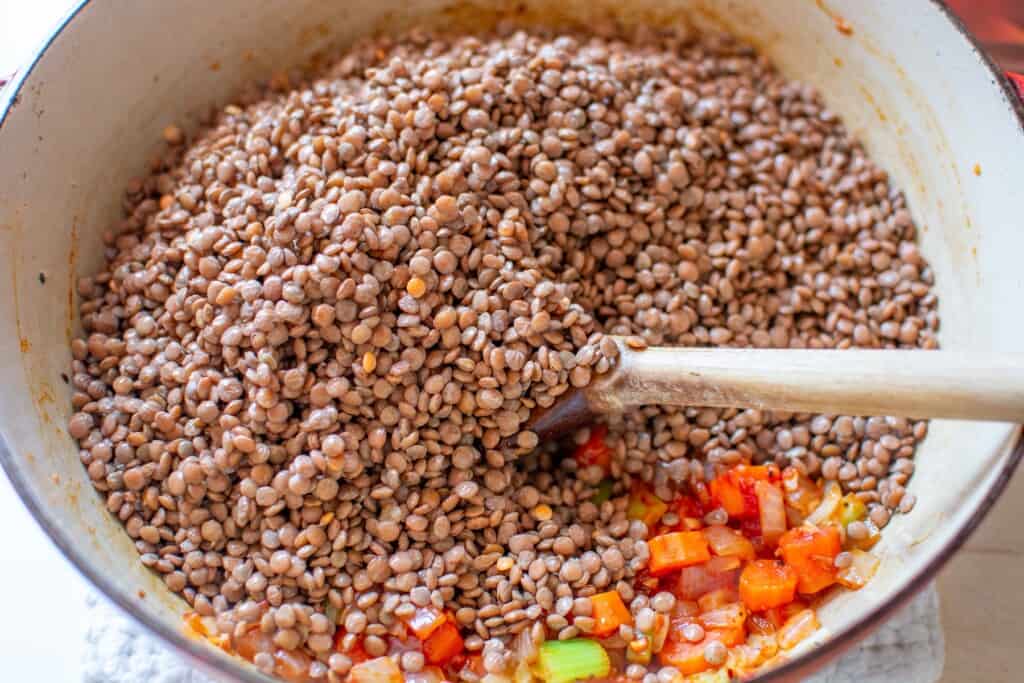 brown lentils in a pot with a wooden spoon