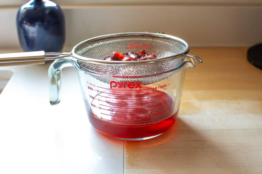 strawberries being strained through a fine mesh strainer