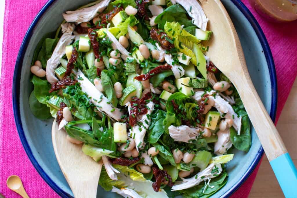 green salad with chicken and two salad servers in it