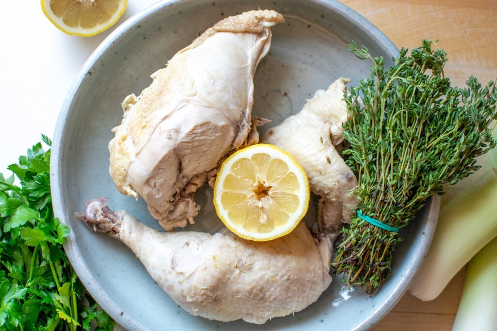 poached chicken on a platter with a lemon half in the middle