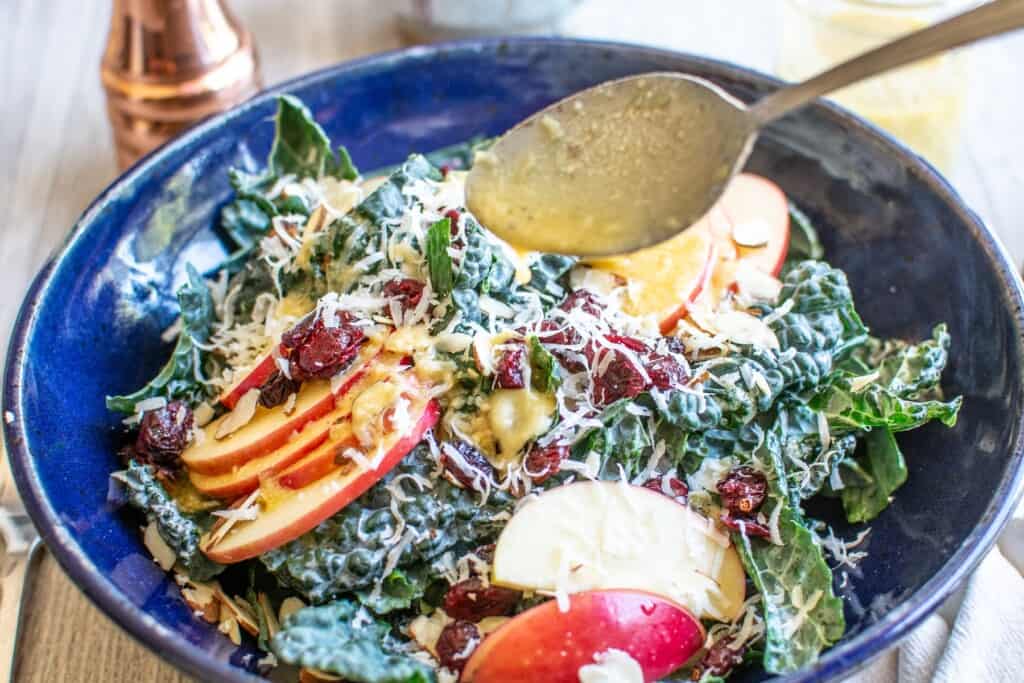 Salad dressing being spooned over a kale salad