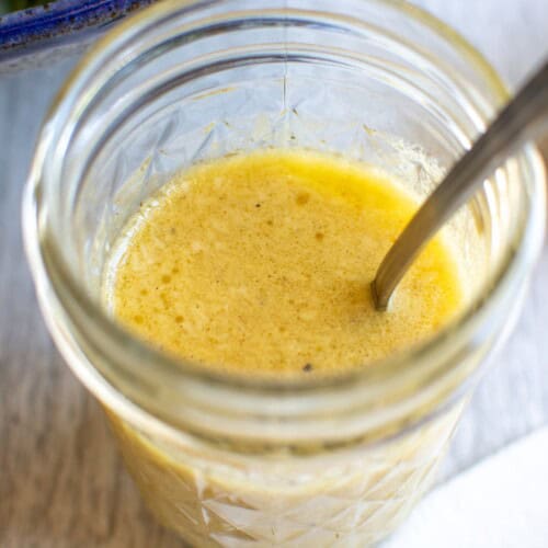 A jar with salad dressing in it and a spoon in the jar